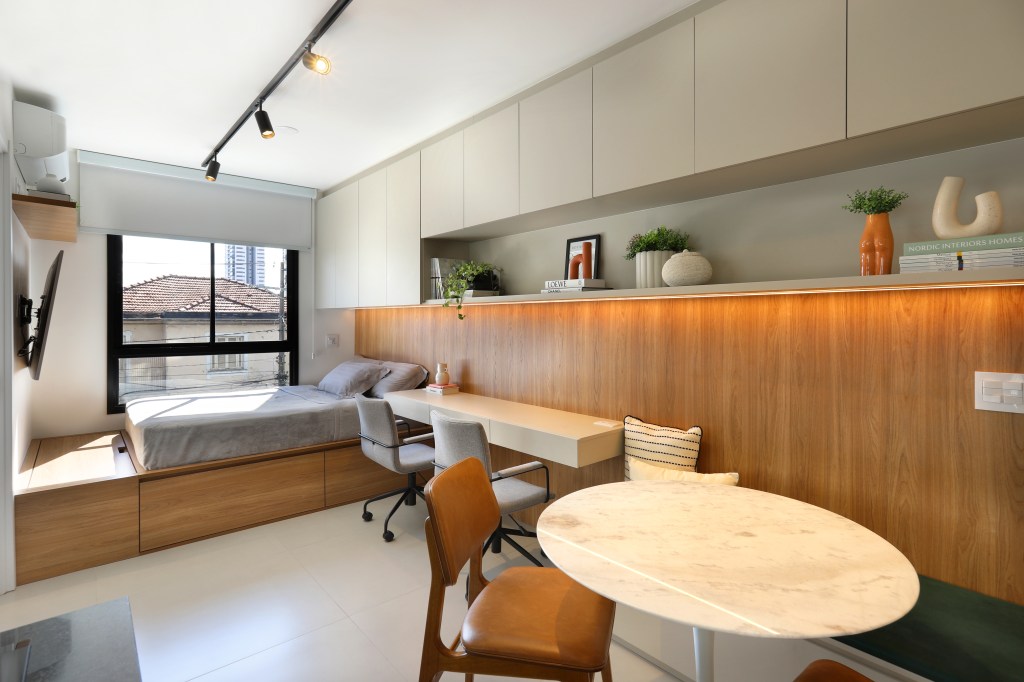 Marcenaria inteligente dá funcionalidade à apê de 42m² com área externa. Projeto de Fantato Nitoli Arquitetura. Na foto, sala de estar integrada com quarto, home office, mesa redonda.