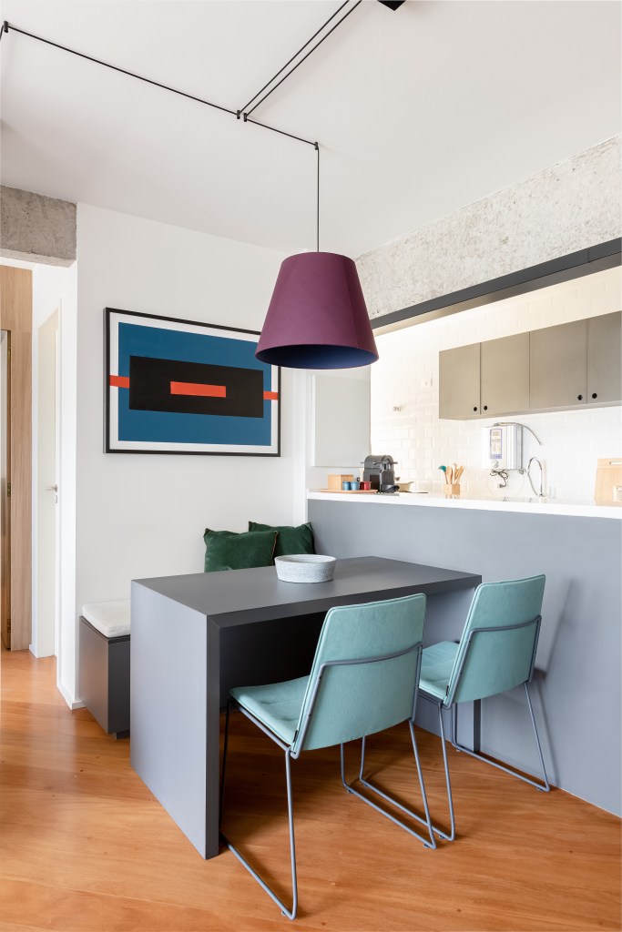 Painel e rack de TV separam living de home office em apê de 75m². Projeto de ISE Arquitetura. Na foto, na sala de jantar pequena com luminária roxa e banco baú.