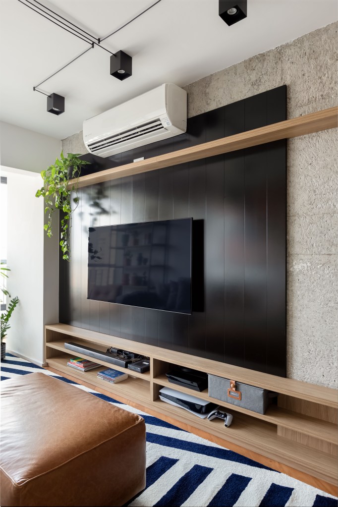 Painel e rack de TV separam living de home office em apê de 75m². Projeto de ISE Arquitetura. Na foto, painel de tv preto e rack.
