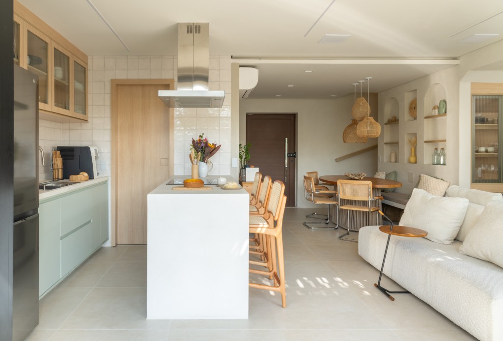 Palhinha, madeira e pedras dão toque boho a esta casa de 130m². Projeto de NOSSA Casa Arquitetura. Na foto, cozinha integrada com bancada branca e marcenaria verde clara.