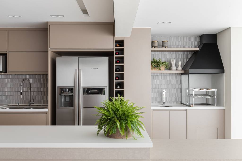 Reforma em apê de 140m² transforma banheiro em biblioteca de home office. Projeto de Blaia e Moura Arquitetos. Na foto, cozinha integrada com sala e varanda gourmet e armários beges.