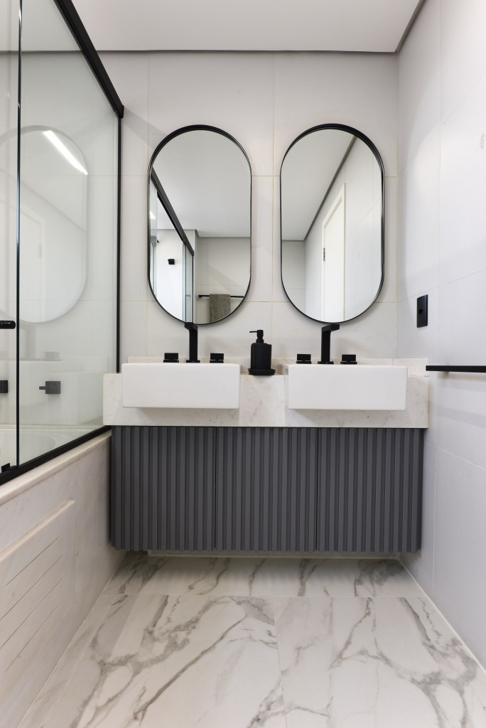 Reforma em apê de 204m² cria área gourmet com mix de granito e MDF. Projeto de AB Palacios Arquitetura. Na foto, banheiro com cuba dupla, espelho oval e armário ripado cinza.