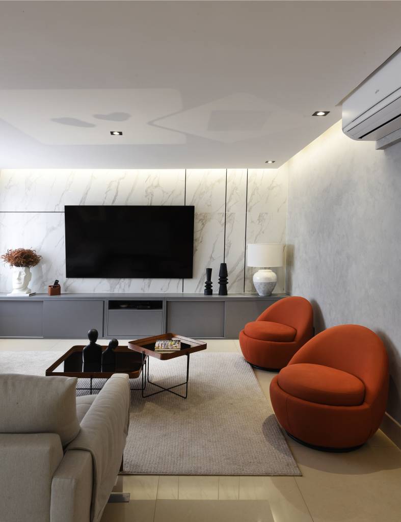 Reforma em apê de 204m² cria área gourmet com mix de granito e MDF. Projeto de AB Palacios Arquitetura. Na foto, sala de tv com sanca iluminada e poltronas laranja.