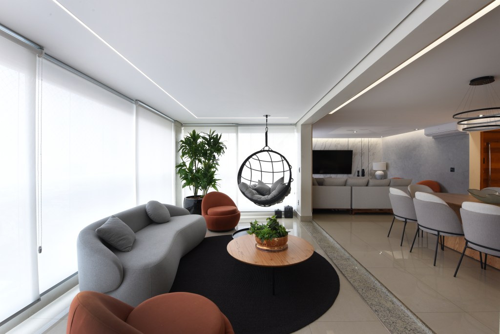 Reforma em apê de 204m² cria área gourmet com mix de granito e MDF. Projeto de AB Palacios Arquitetura. Na foto, sala de estar com sofá curvo, balanço, tapete azul escuro.