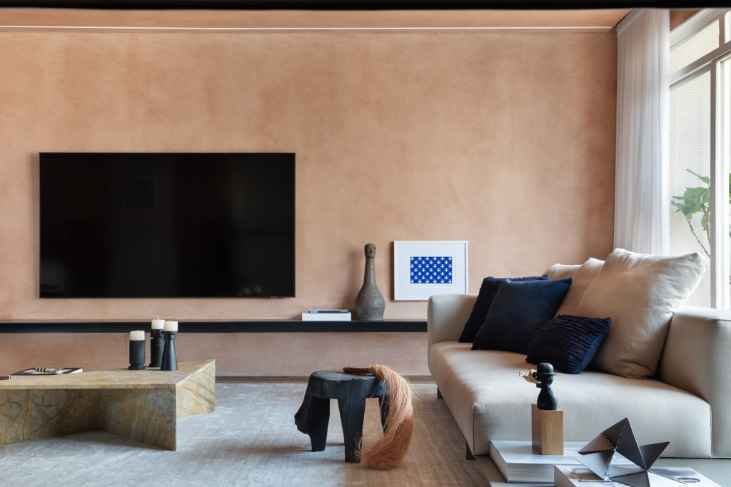 Textura terrosa nas paredes marca o décor deste apê de 220 m². Projeto de Navarro Arquitetura. Na foto, sala de estar com tv, mesa de pedra a parede terrosa.