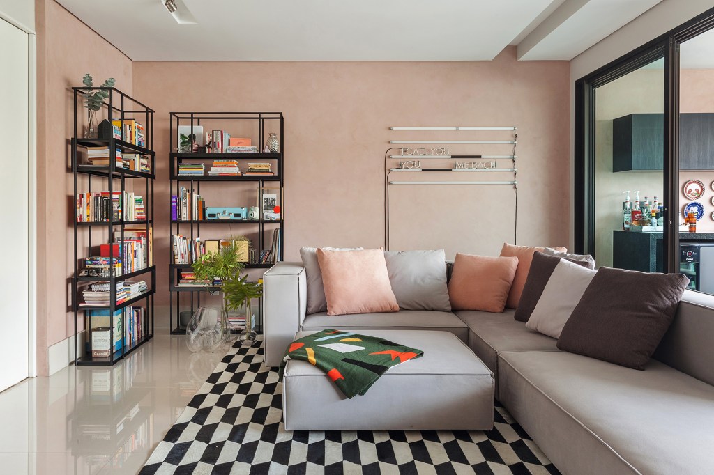Tons de rosa marcam apê inspirado nos lofts nova-iorquinos. Projeto de Dubal Arquitetura. Na foto. sala com sofá em L, estante de serralheria, neon e parede rosa.