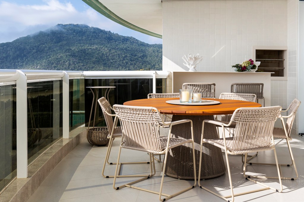 Varanda generosa com vista para o mar é destaque em apê de 160m². Projeto de SUM + Studio. Na foto, varanda com mesa redonda de madeira com cadeiras e vista para o mar.