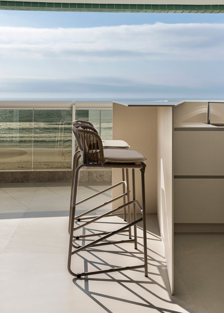 Varanda generosa com vista para o mar é destaque em apê de 160m². Projeto de SUM + Studio. Na foto, varanda com bancada de churrasqueira.