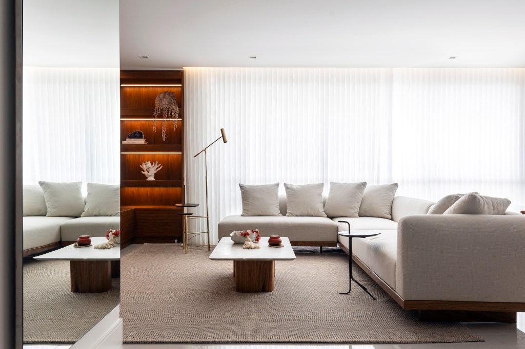 Varanda generosa com vista para o mar é destaque em apê de 160m². Projeto de SUM + Studio. Na foto, sala de estar minimalista com sofá L branco e tapete bege.