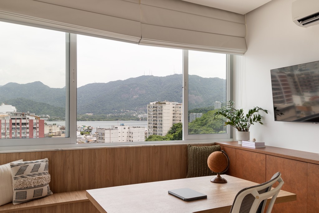 Vigas, reboco aparente e texturas artesanais marcam este apê de 130 m². Projeto de Mariana Monnerat. Na foto, escritório com banco e tv.