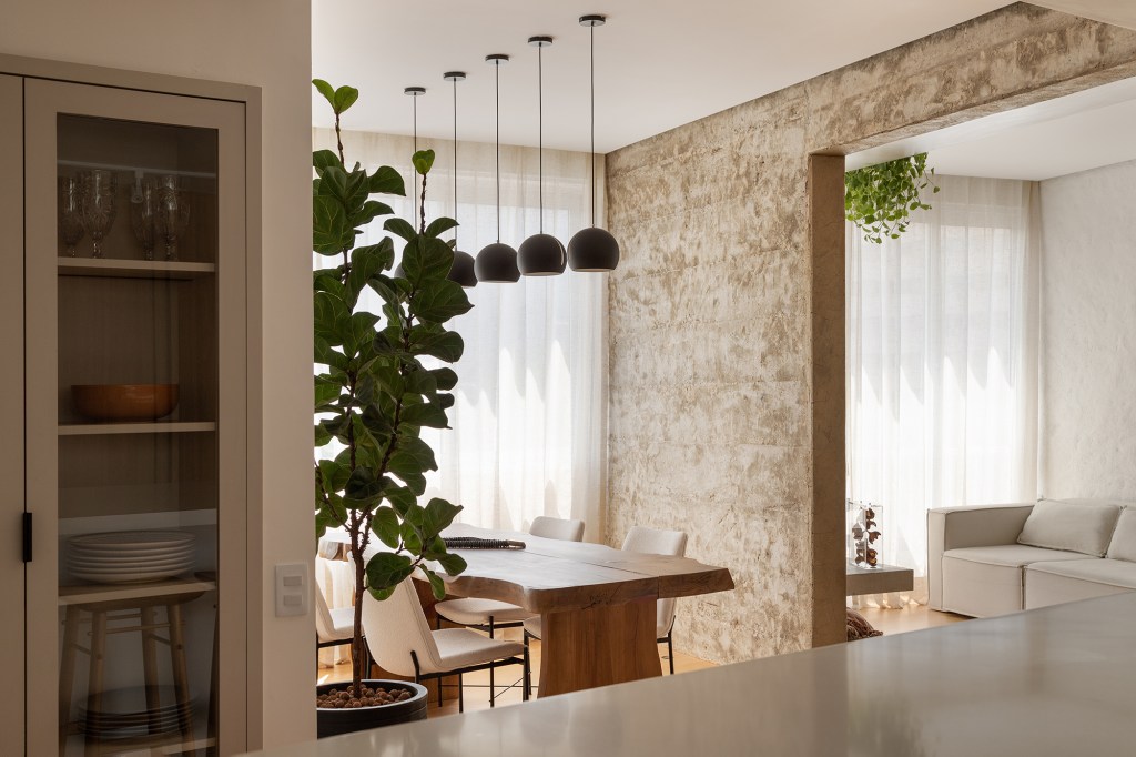 Vigas, reboco aparente e texturas artesanais marcam este apê de 130 m². Projeto de Mariana Monnerat. Na foto, sala de jantar com parede texturizada e cristaleira.