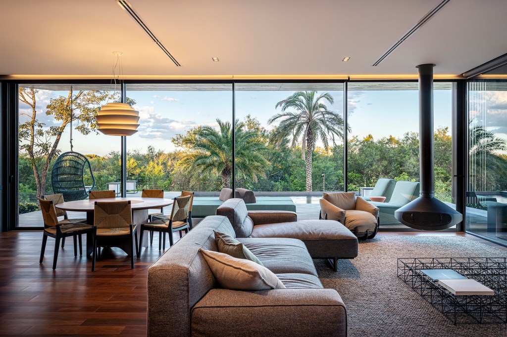A água é destaque nesta casa de 457 m² no Rio Grande do Sul. Projeto de Stemmer Rodrigues. Na foto, sala de estar e jantar com vista para a piscina e lareira.