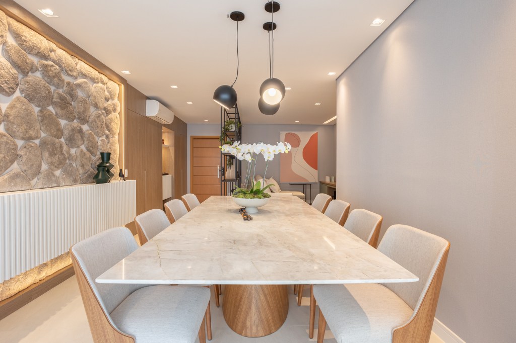 Apartamento de 140 m² possui parede de pedra moledo e quarto montessoriano. Projeto Loft 7 Arquitetura. Na foto, sala de jantar com parede de pedra e mesa de mármore.