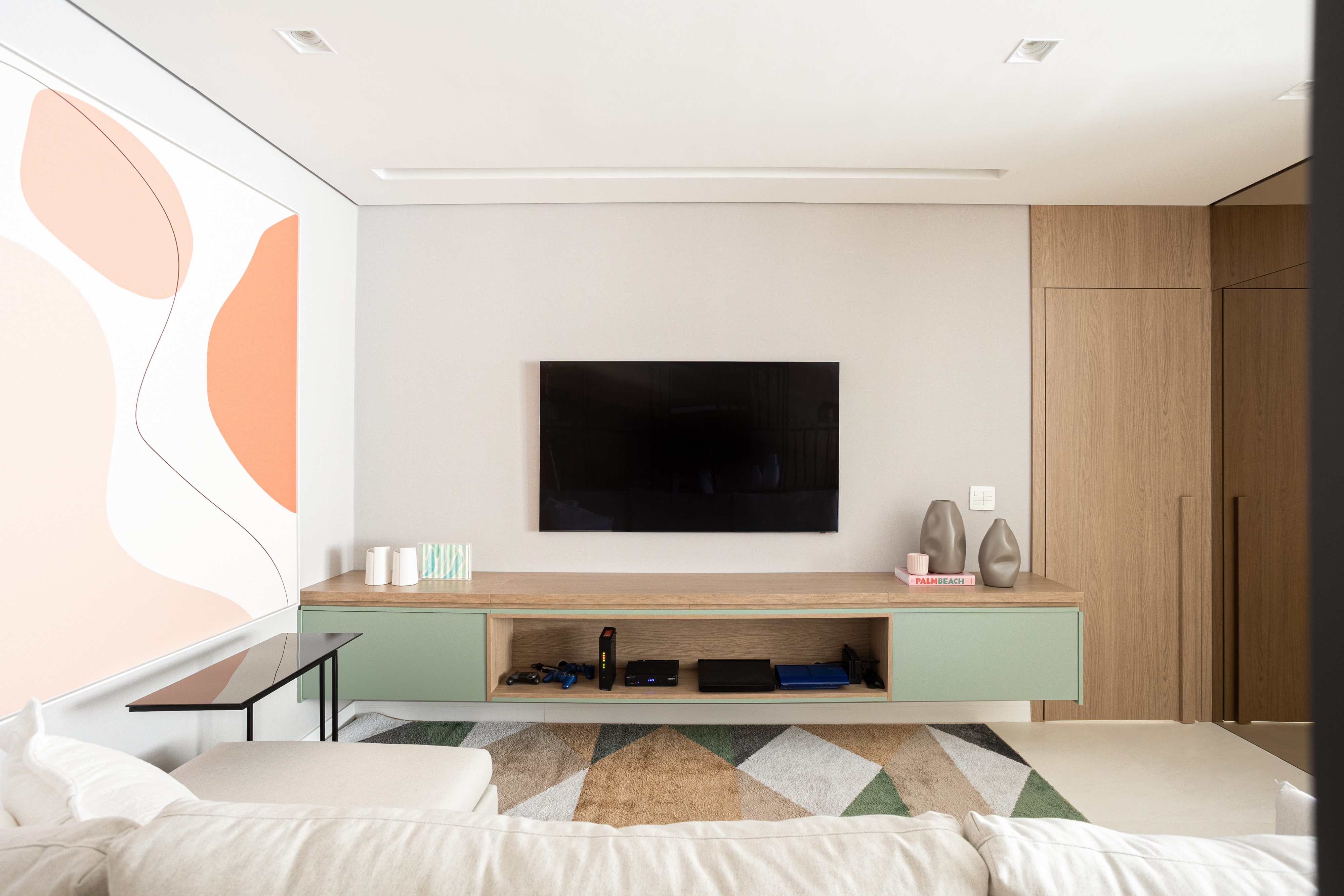 Apartamento de 140 m² possui parede de pedra moledo e quarto montessoriano. Projeto Loft 7 Arquitetura. Na foto, sala de tv com tapete colorido e quadro.