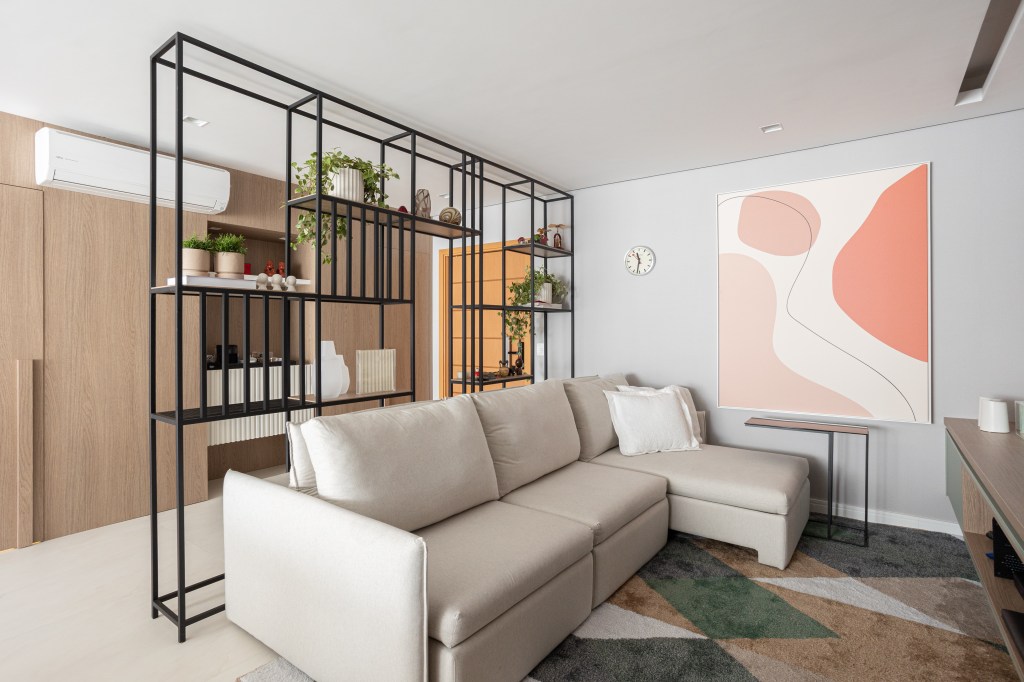 Apartamento de 140 m² possui parede de pedra moledo e quarto montessoriano. Projeto Loft 7 Arquitetura. Na foto, sala de TV com estante de serralheria e tapete colorido.