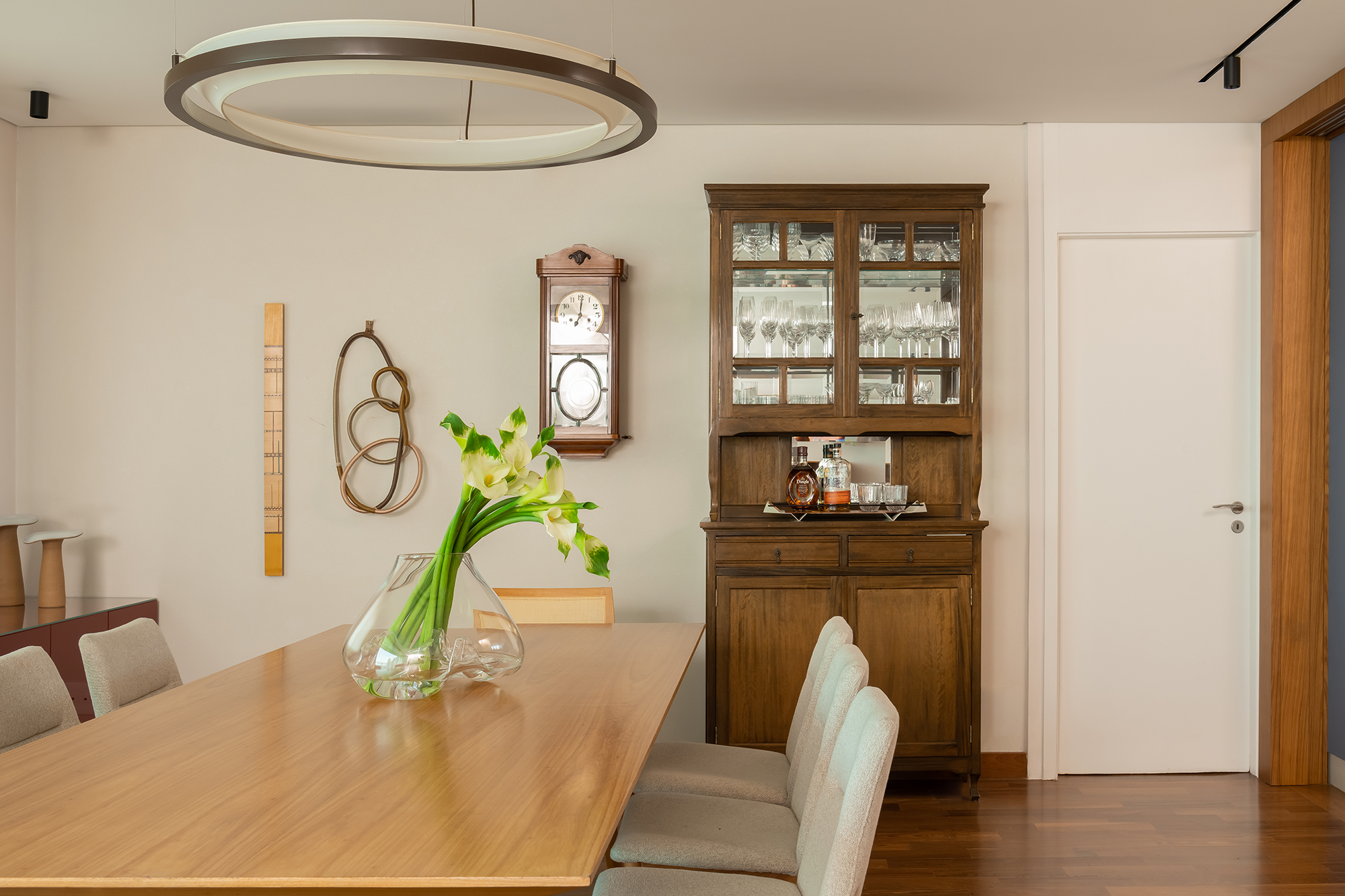 Apartamento de 188 m² ganha dois cooktops na cozinha e balanços na sala, Projeto Raízes Arquitetos. Na foto, sala de jantar com cristaleira e relógio antigo.