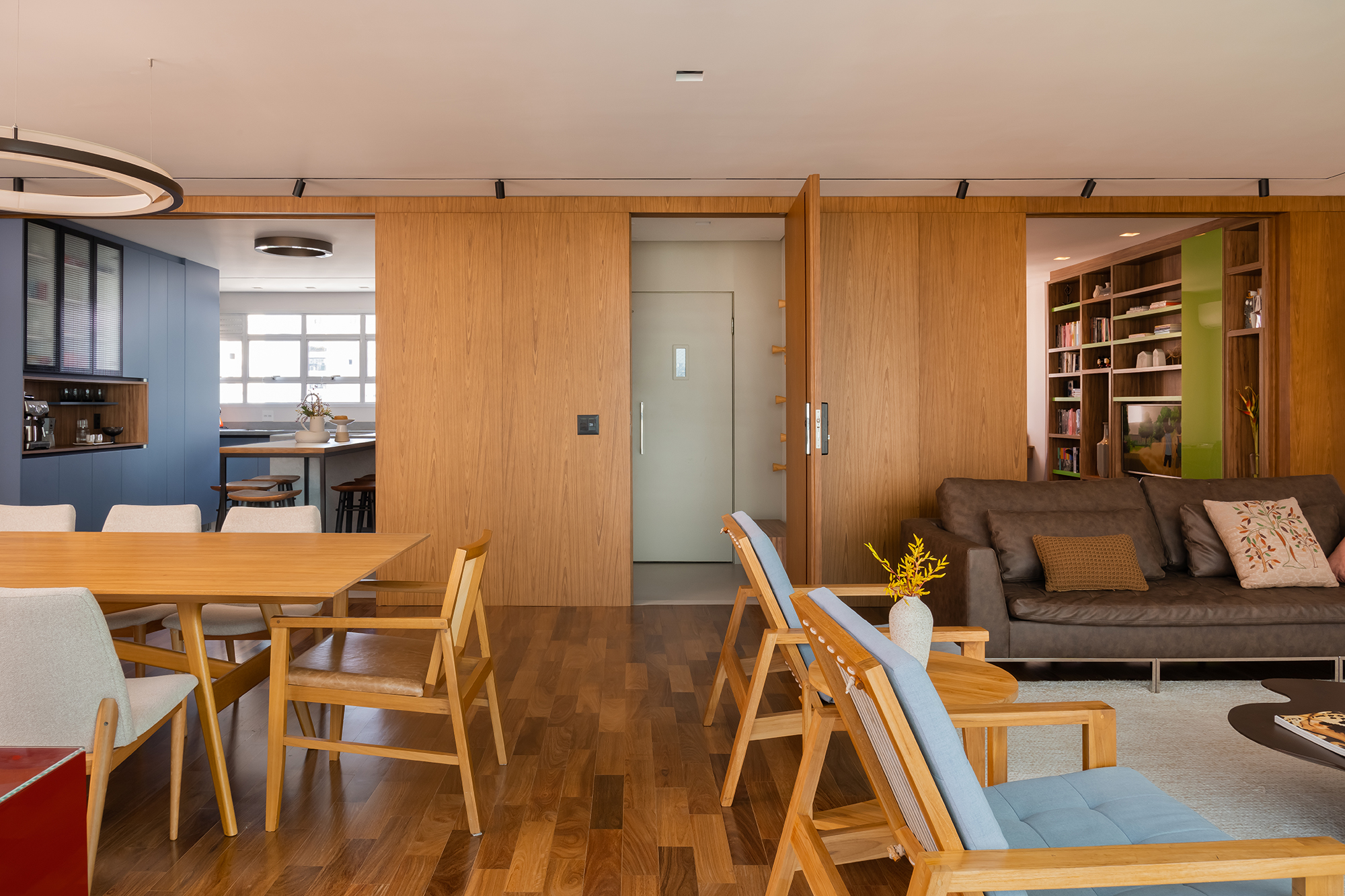 Apartamento de 188 m² ganha dois cooktops na cozinha e balanços na sala, Projeto Raízes Arquitetos. Na foto, salas de estar e jantar integradas com a cozinha. Painéis de madeira na parede,