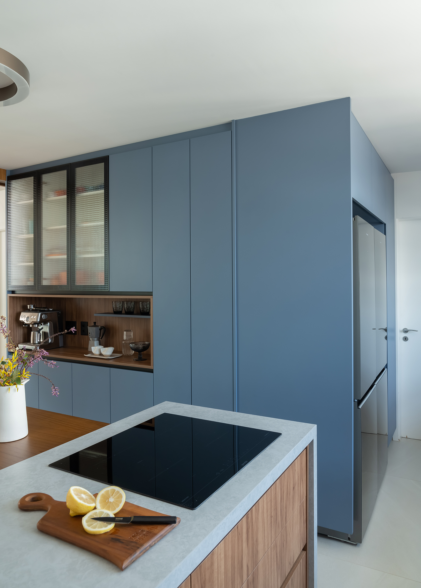Apartamento de 188 m² ganha dois cooktops na cozinha e balanços na sala, Projeto Raízes Arquitetos. Na foto, cozinha com marcenaria azul e ilha. Cooktop e nicho para café.