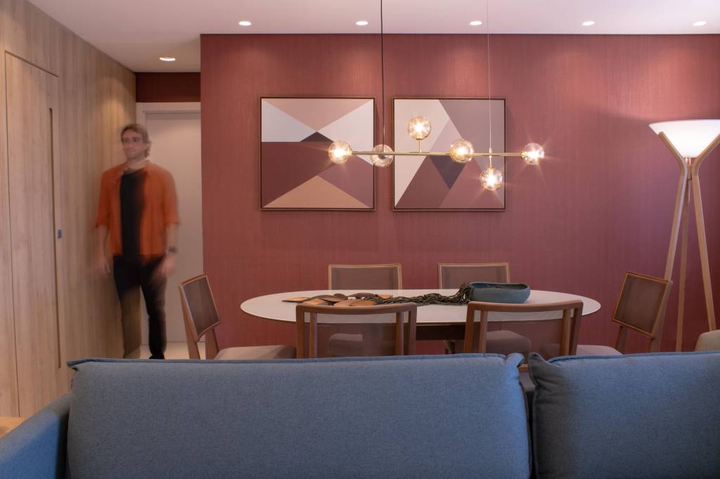 Apartamento de 80 m² ganha lareira a gás e parede marsala na sala. Projeto do arquiteto Felippe Comninos, à frente da Vale Arquitetura, em parceria com a arquiteta Adriana Marcassa Cotrin, do escritório Marcassa Cotrin. Na foto, sala de jantar com quadros e parede marsala.