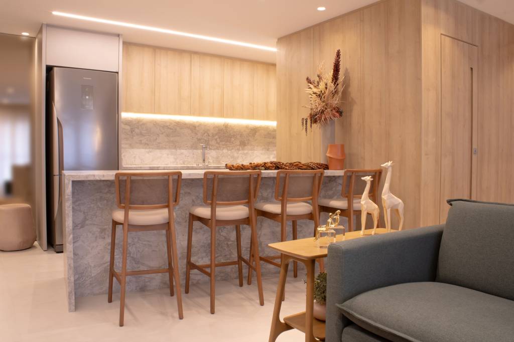 Apartamento de 80 m² ganha lareira a gás e parede marsala na sala. Projeto do arquiteto Felippe Comninos, à frente da Vale Arquitetura, em parceria com a arquiteta Adriana Marcassa Cotrin, do escritório Marcassa Cotrin. Na foto, sala com cozinha americana e balcão com textura de pedra.