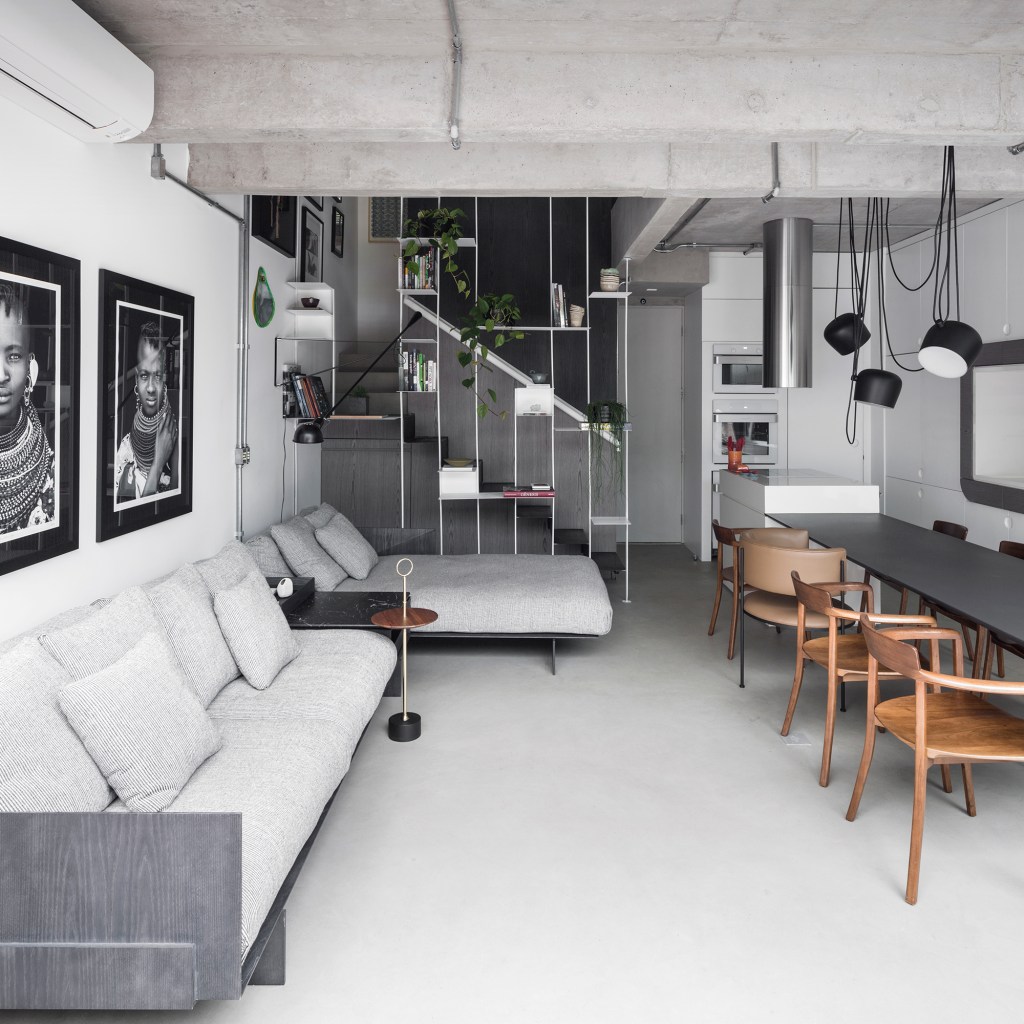 Apartamento garden de 100 m² mescla materiais para criar um ar industrial. Projeto de Nati Minas. Na foto, sala com estante vazada, escada e quadros.