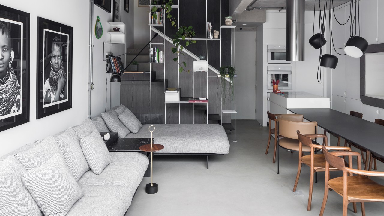 Apartamento garden de 100 m² mescla materiais para criar um ar industrial. Projeto de Nati Minas. Na foto, sala com estante vazada, escada e quadros.