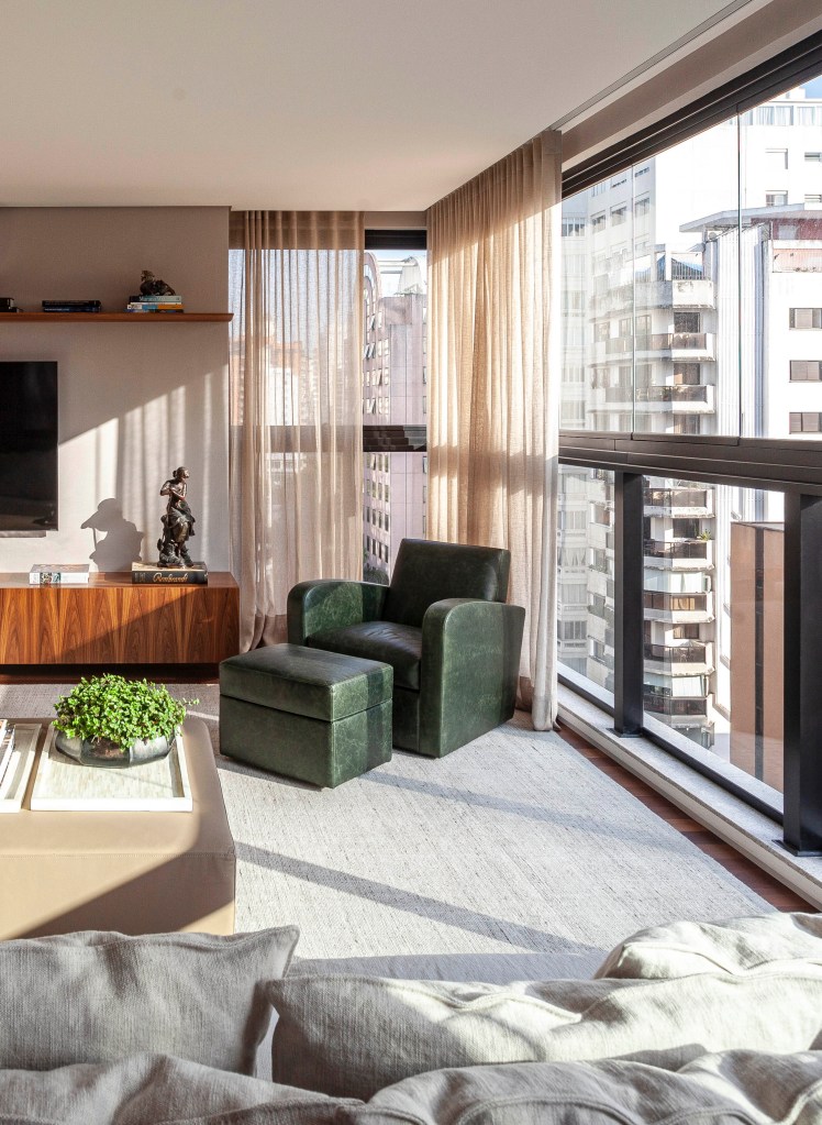 Apê de 174 m² tem decoração clássica e sofisticada com tons neutros. Projeto de David Bastos. Na foto, sala de estar com varanda integrada, cortina e poltrona verde.