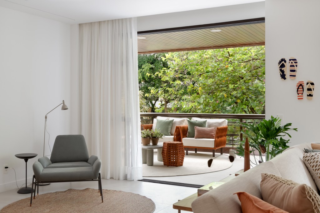 Apê de 230 m² ganha décor com tons terrosos e ilha de cozinha com reforma. Projeto de Paula Muller. Na foto, sala, varanda, cortina branca, poltrona verde.