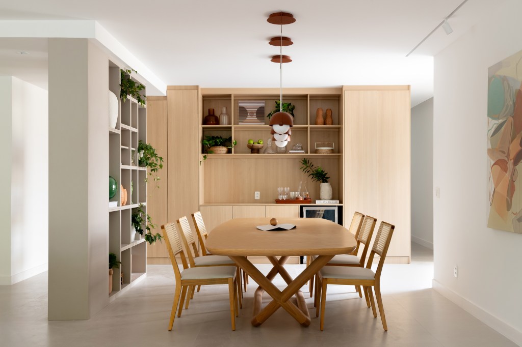 Apê de 230 m² ganha décor com tons terrosos e ilha de cozinha com reforma. Projeto de Paula Muller. Na foto, sala de jantar com mesa de madeira, estante de nichos.
