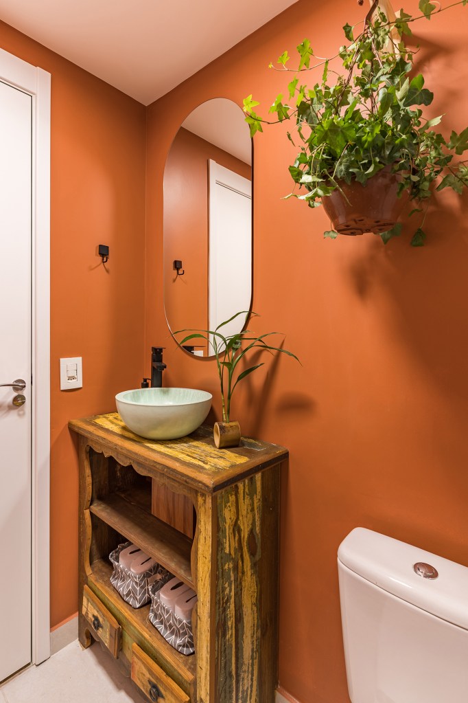 Apê de 62 m² une estilo praiano com toques industriais. Projeto de Letícia de Nóbrega. Na foto, lavabo com bancada de madeira e parede laranja.