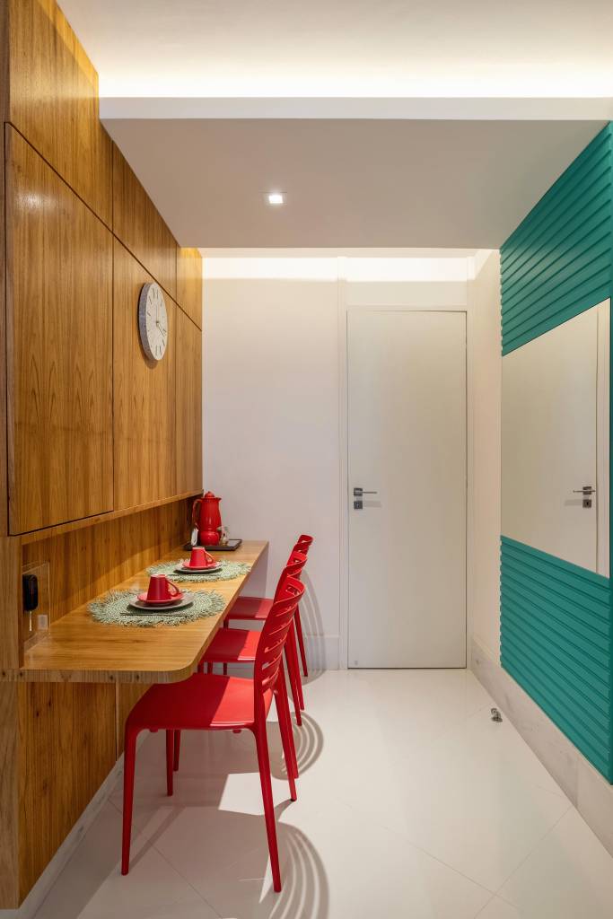 Apê ganha mezanino com home office, lavabo azul e copa de cozinha turquesa. Projeto de Ana Cano Arquitetura. Na foto, copa de cozinha com painel turquesa, parede revestida de madeira, cadeiras vermelhas.