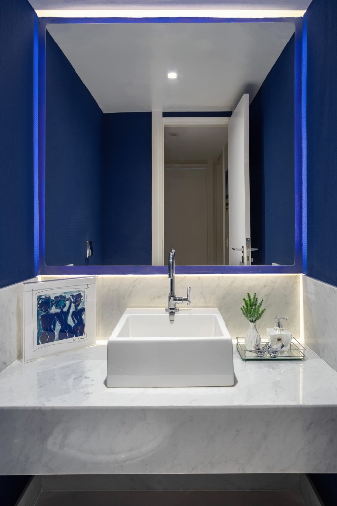 Apê ganha mezanino com home office, lavabo azul e copa de cozinha turquesa. Projeto de Ana Cano Arquitetura. Na foto, lavabo azul com espelho iluminado.