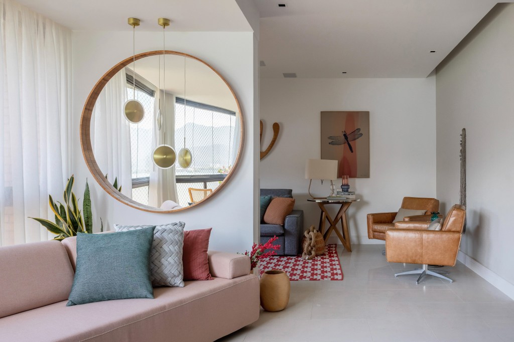 Apê ganha mezanino com home office, lavabo azul e copa de cozinha turquesa. Projeto de Ana Cano Arquitetura. Na foto, sala de estar, sofá rosa claro, espelho redondo.