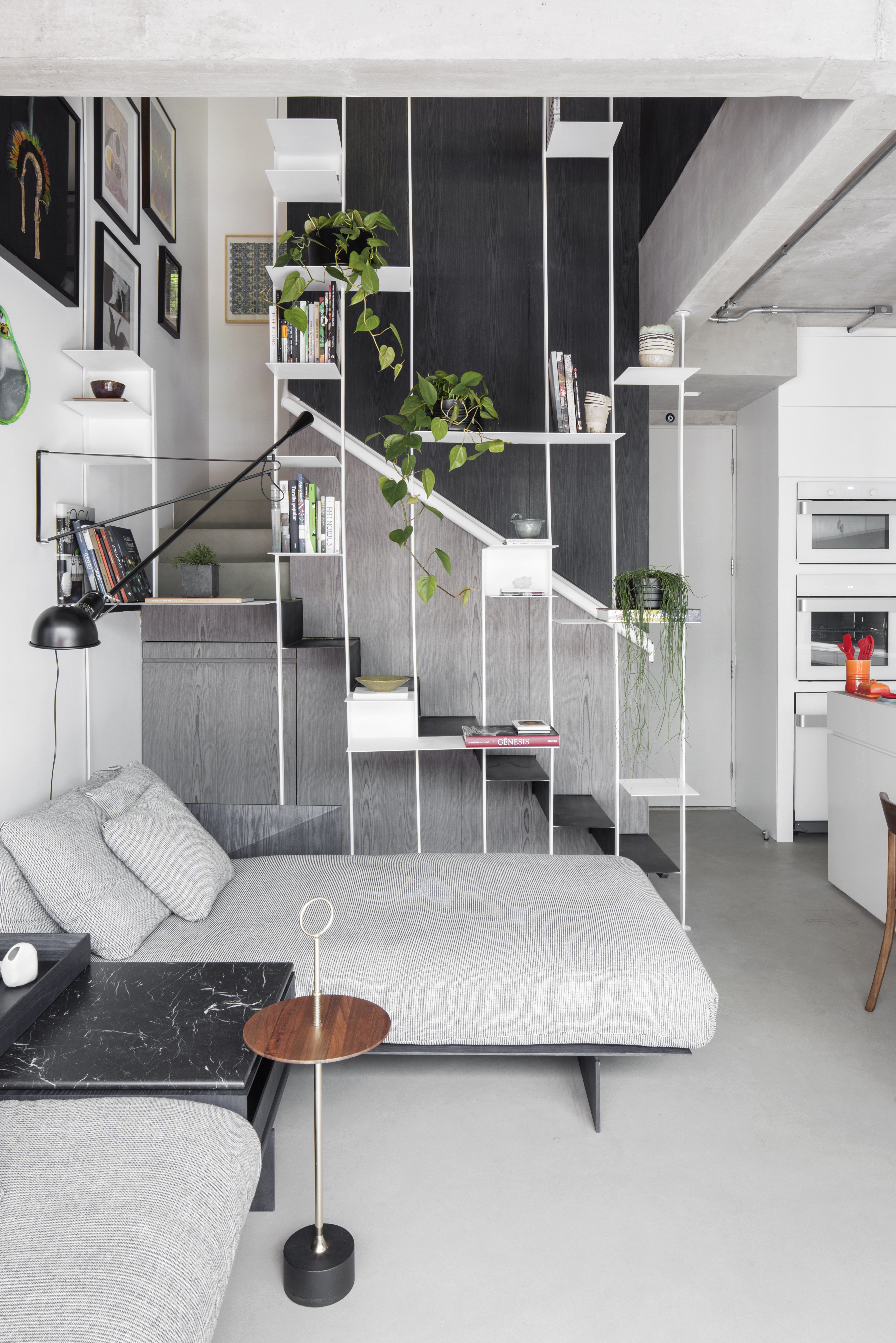 Apê térreo preto e branco tem áreas sociais e de trabalho mescladas. Projeto de Nati Minas & Studio. Na foto, sofá cinza, escada com guarda corpo vazado com plantas.