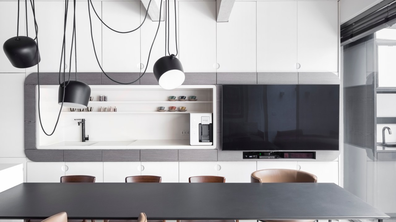 Apê térreo preto e branco tem áreas sociais e de trabalho mescladas. Projeto de Nati Minas & Studio. Na foto, cozinha integrada, luminária preta, mesa preta, marcenaria branca.