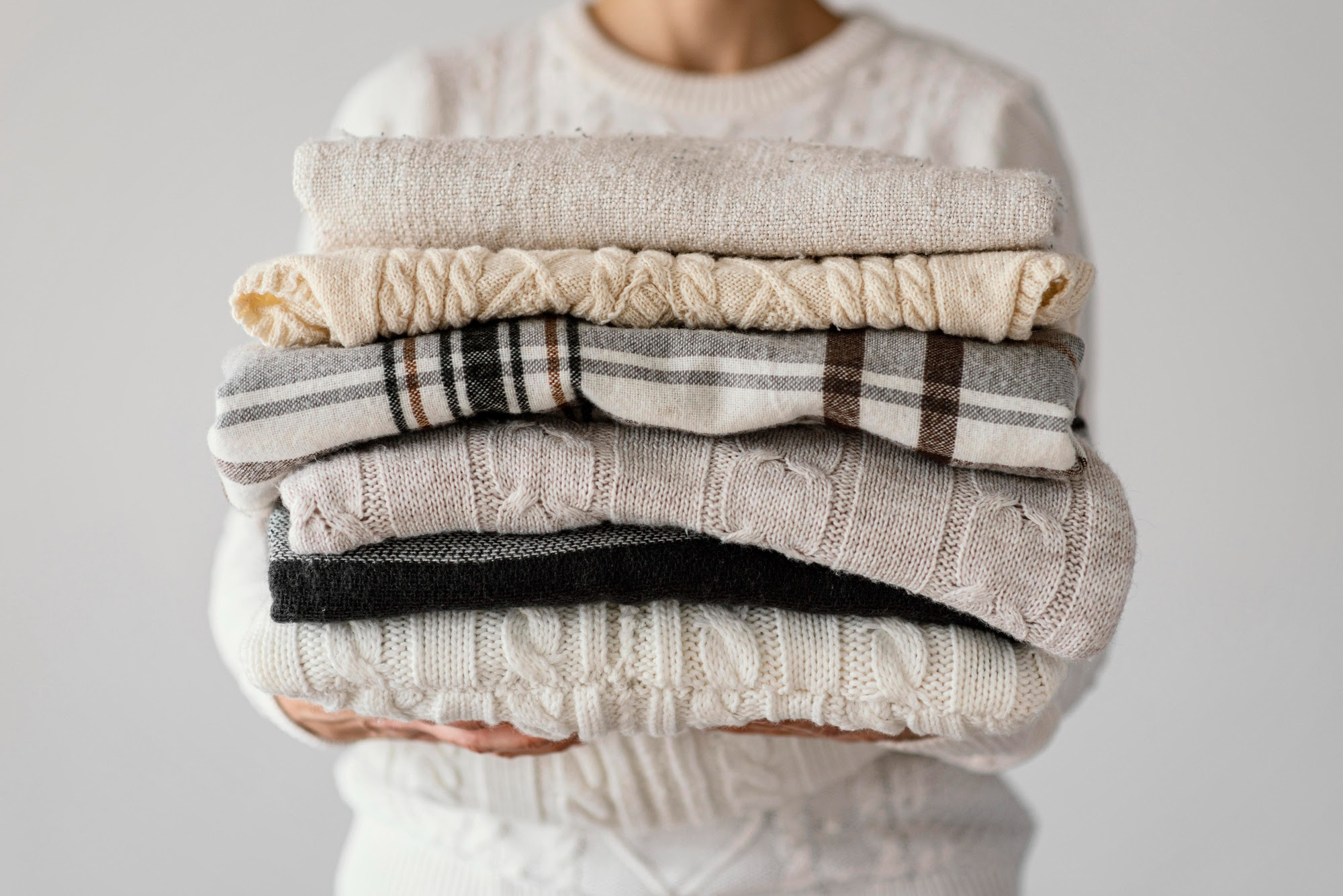 Aproveite o calor para lavar edredons e roupas de inverno! Confira dicas. Na foto, pessoa carregando roupas e cobertores.