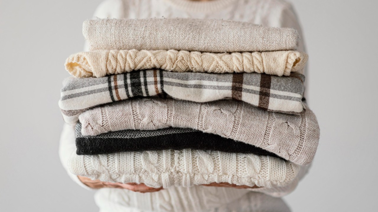Aproveite o calor para lavar edredons e roupas de inverno! Confira dicas. Na foto, pessoa carregando roupas e cobertores.