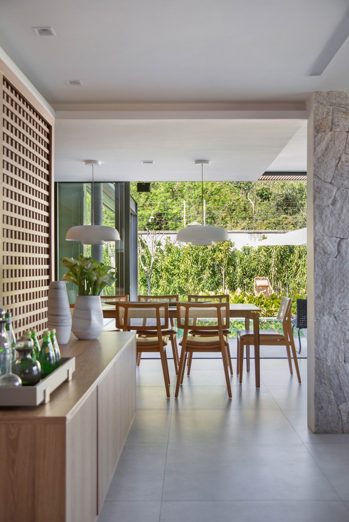 Casa de 300 m² tem cozinha verde oliva e área gourmet em contêiner. Projeto de Lana Rocha. Na foto, sala de jantar com grandes janelas para jardim.