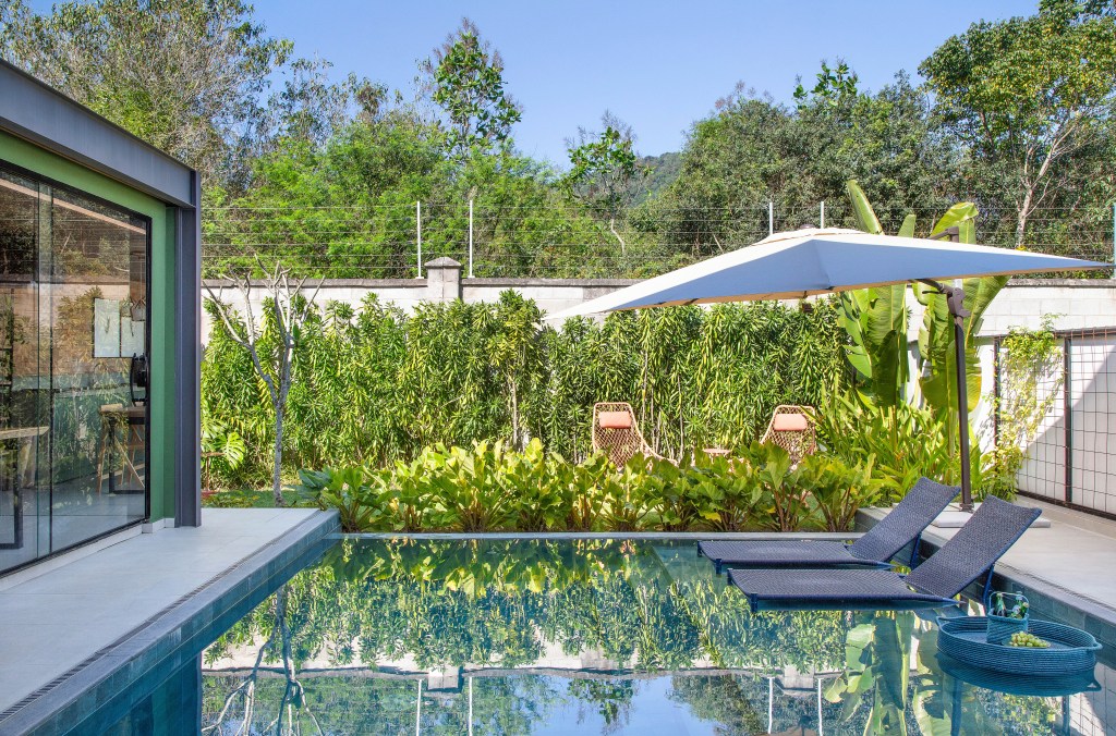Casa de 300 m² tem cozinha verde oliva e área gourmet em contêiner. Projeto de Lana Rocha. Na foto, área externa com piscina e folhagens. Jardim.