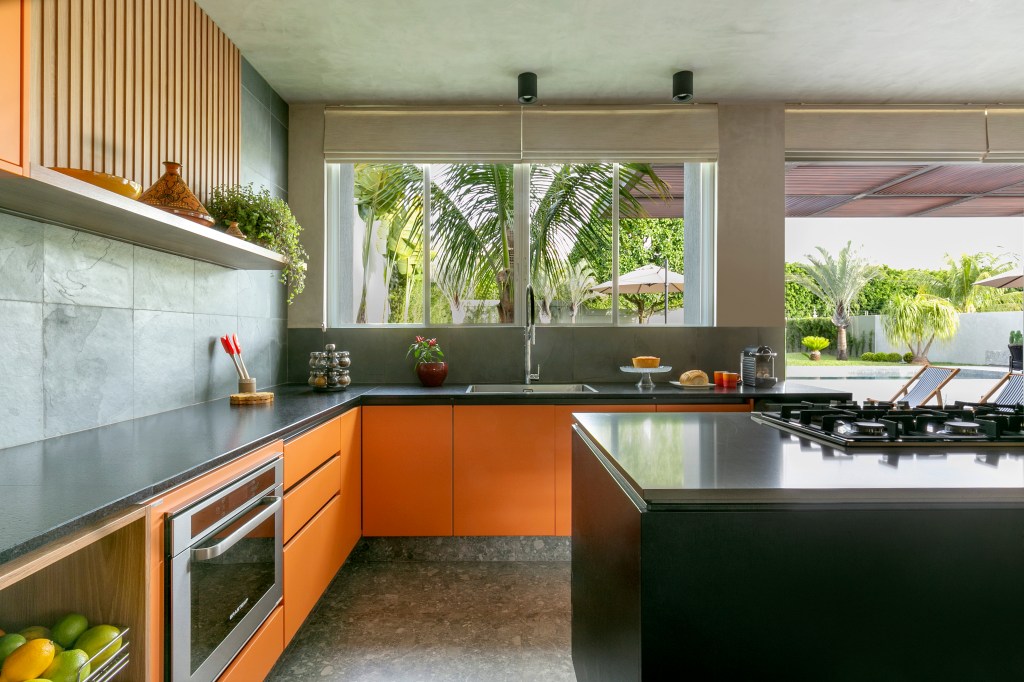 Casa ganha área gourmet e cozinha com marceneira laranja e ardósia. Projeto de Morada 3112 Arquitetura. Na foto, cozinha, parede com ardósia, armário laranja.
