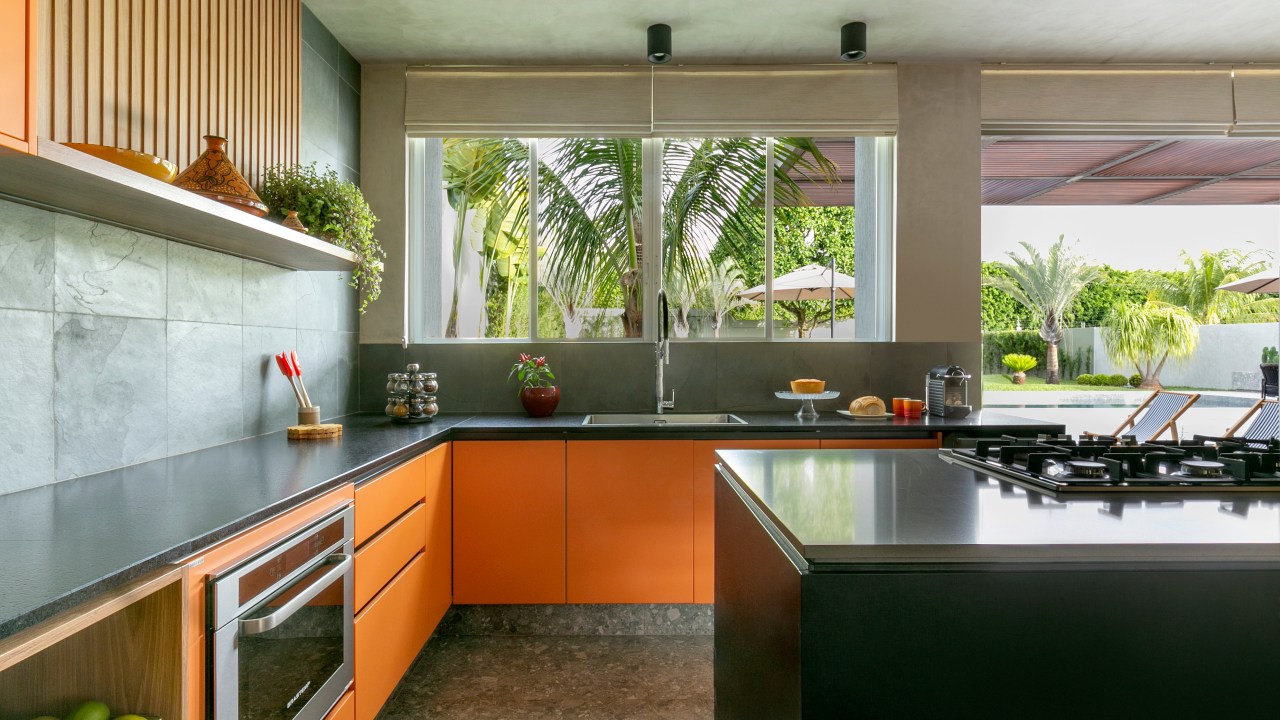Casa ganha área gourmet e cozinha com marceneira laranja e ardósia. Projeto de Morada 3112 Arquitetura. Na foto, cozinha, parede com ardósia, armário laranja.