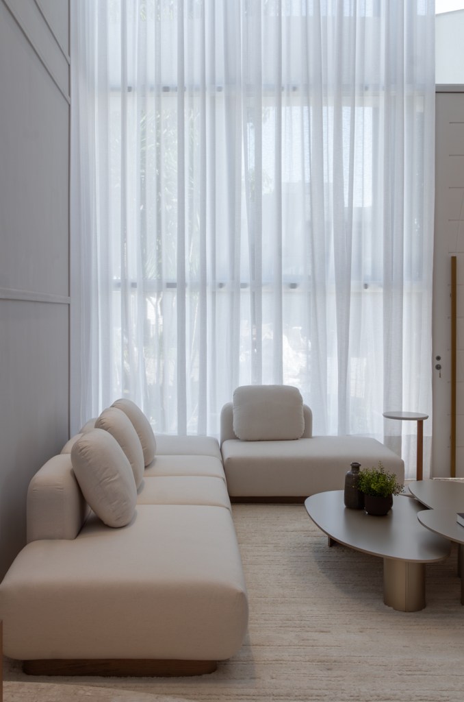 Casa do zagueiro da seleção Gleison Bremer tem estilo minimalista elegante. Projeto de Daniel Santana. Na foto, sala de estar com pé-direito duplo, cortina branca e sofá branco.