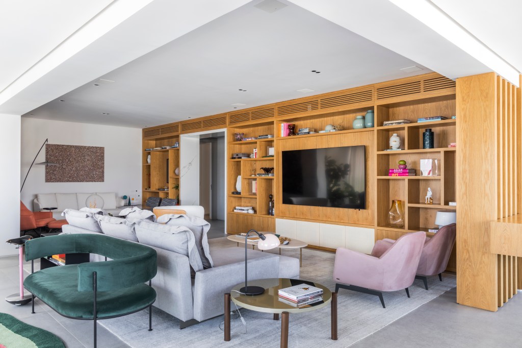Contemporâneo e atemporal: apê tem varanda integrada e tons neutros. Projeto de BZP Arquitetura. Na foto, sala de estar com sofá cinza, poltrona rosa, poltrona verde, estante de marcenaria.