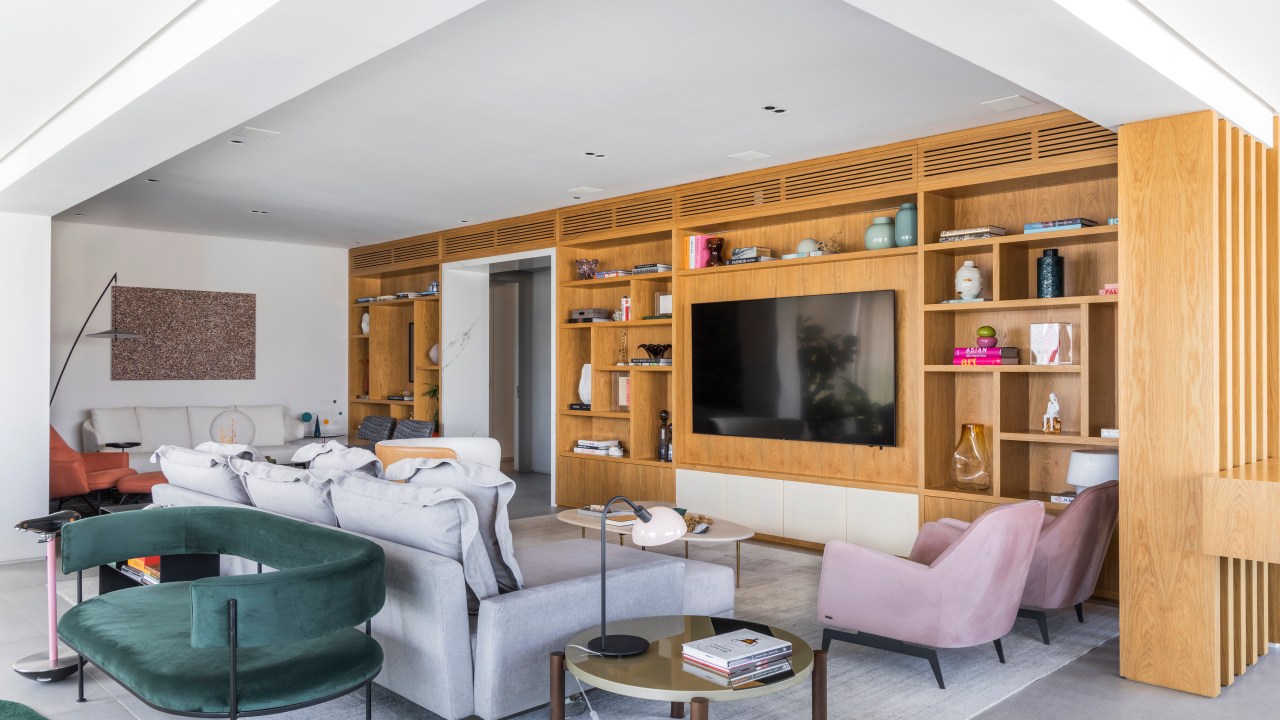 Contemporâneo e atemporal: apê tem varanda integrada e tons neutros. Projeto de BZP Arquitetura. Na foto, sala de estar com sofá cinza, poltrona rosa, poltrona verde, estante de marcenaria.