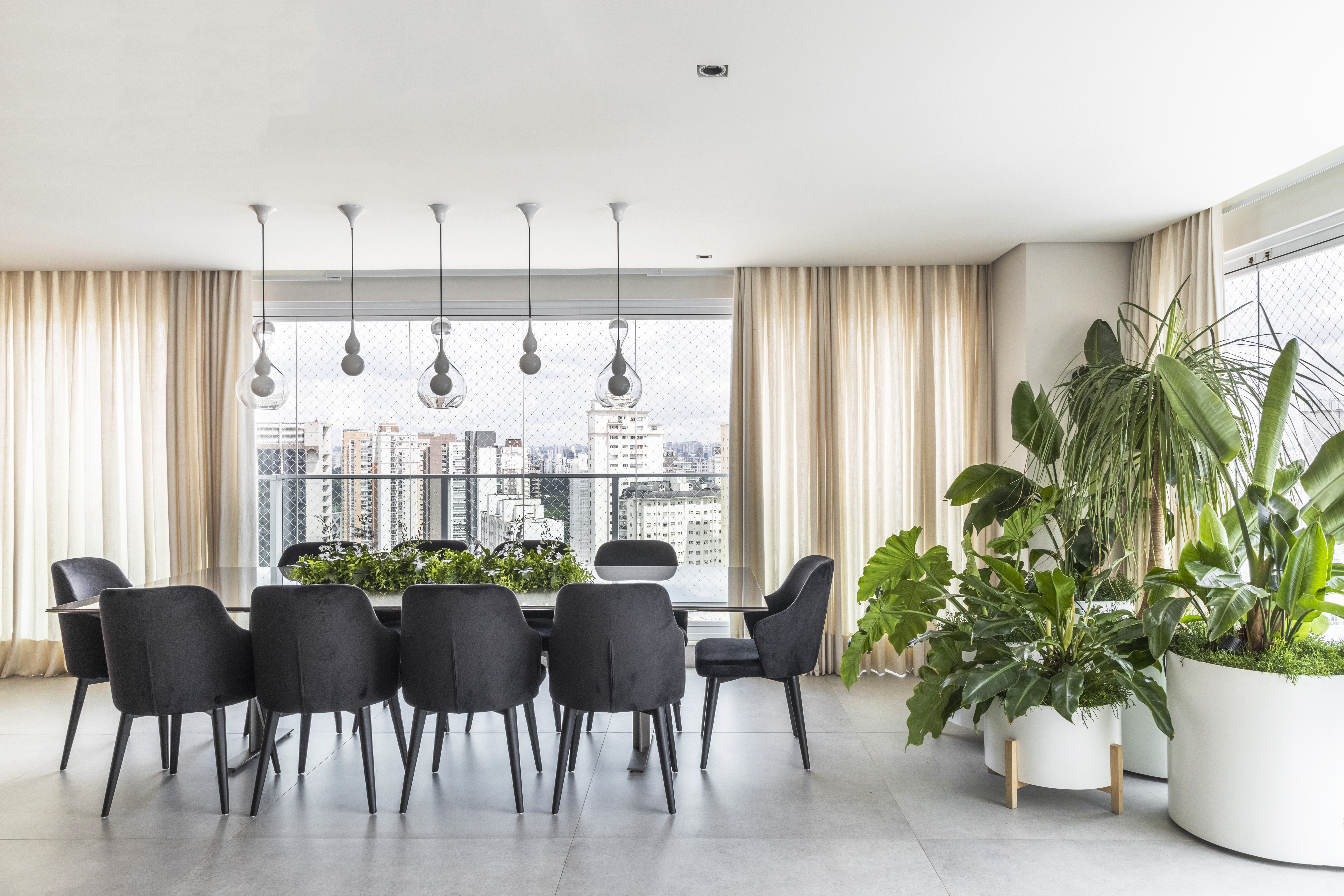 Contemporâneo e atemporal: apê tem varanda integrada e tons neutros. Projeto de BZP Arquitetura. Na foto, sala de jantar com cadeiras pretas estofadas e plantas na mesa e no canto da sala.