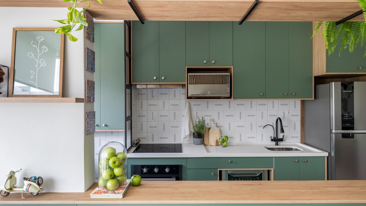 Cozinha verde e granilite no banheiro marca apartamento de 58 m². Projeto de Pixel Arquitetura. Na foto, cozinha americana com marcenaria verde e prateleiras.