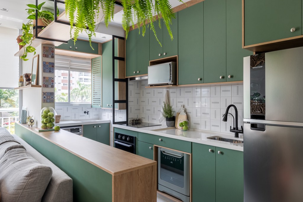 Cozinha verde e granilite no banheiro marca apartamento de 58 m². Projeto de Pixel Arquitetura. Na foto, cozinha americana com marcenaria verde e lavanderia integrada.