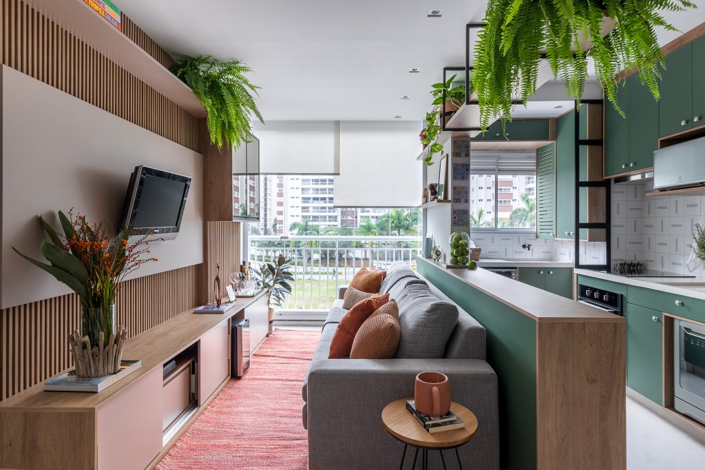 Cozinha verde e granilite no banheiro marca apartamento de 58 m². Projeto de Pixel Arquitetura. Na foto, sala com cozinha integrada e marcenaria verde, Painel de Tv ripado.
