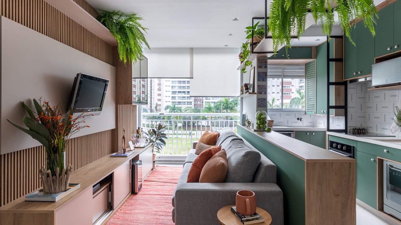 Cozinha verde e granilite no banheiro marca apartamento de 58 m². Projeto de Pixel Arquitetura. Na foto, sala com cozinha integrada e marcenaria verde, Painel de Tv ripado.