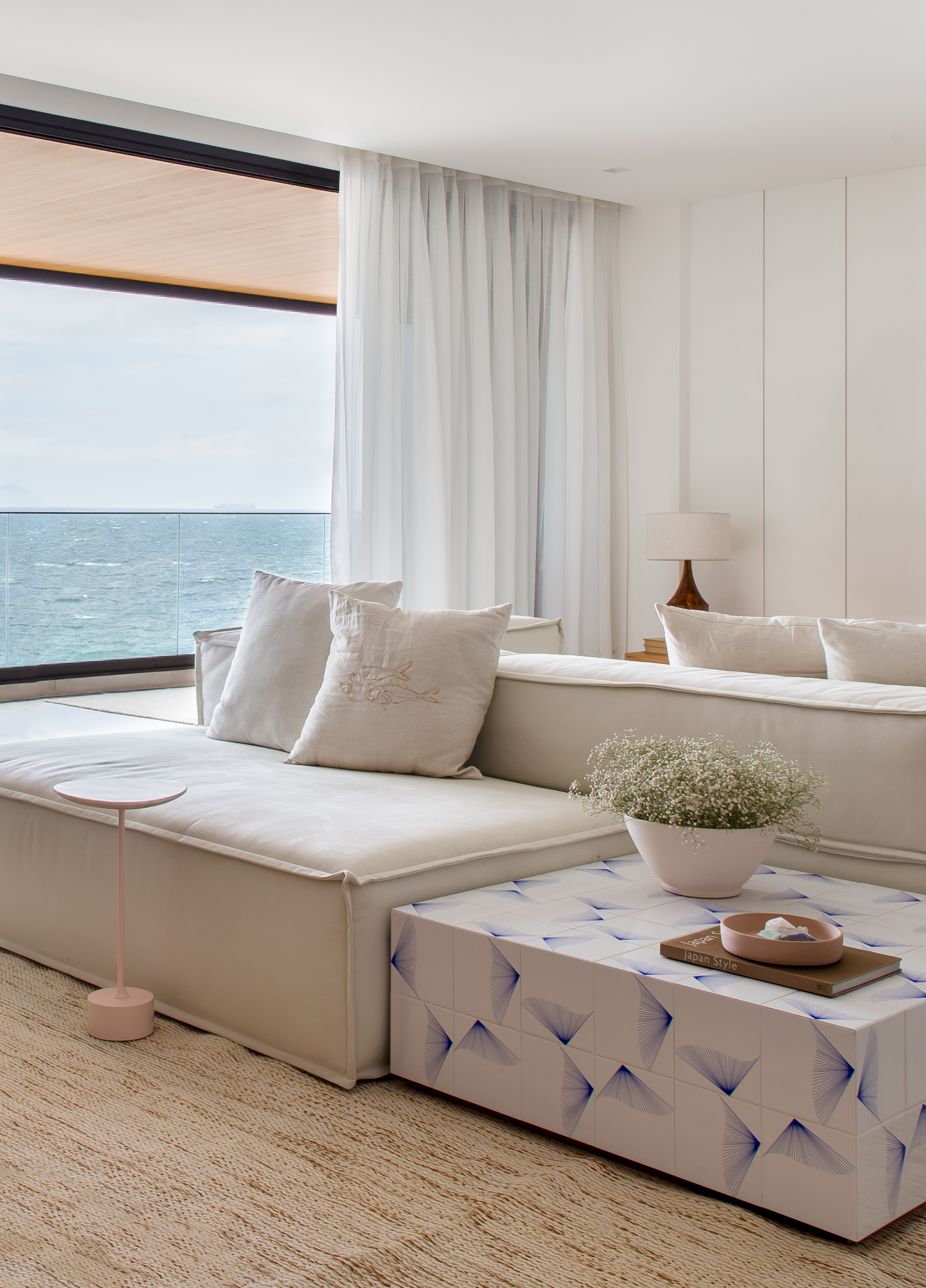 Décor essencial com branco e madeira peroba valoriza o mar neste apê. Projeto de PKB Arquitetura. Na foto, sala de estar, sofá branco ilha, mesa de centro com azulejos.